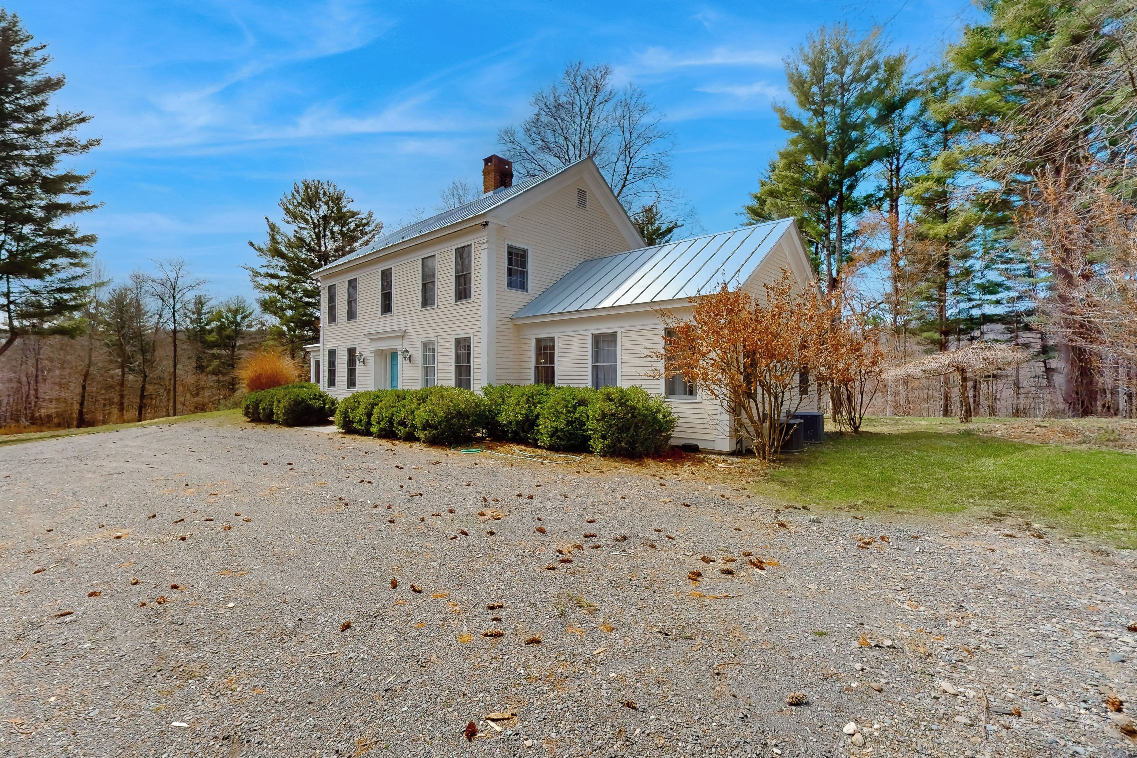 A two-story house with a metal roof, surrounded by a gravel driveway and a small lawn.