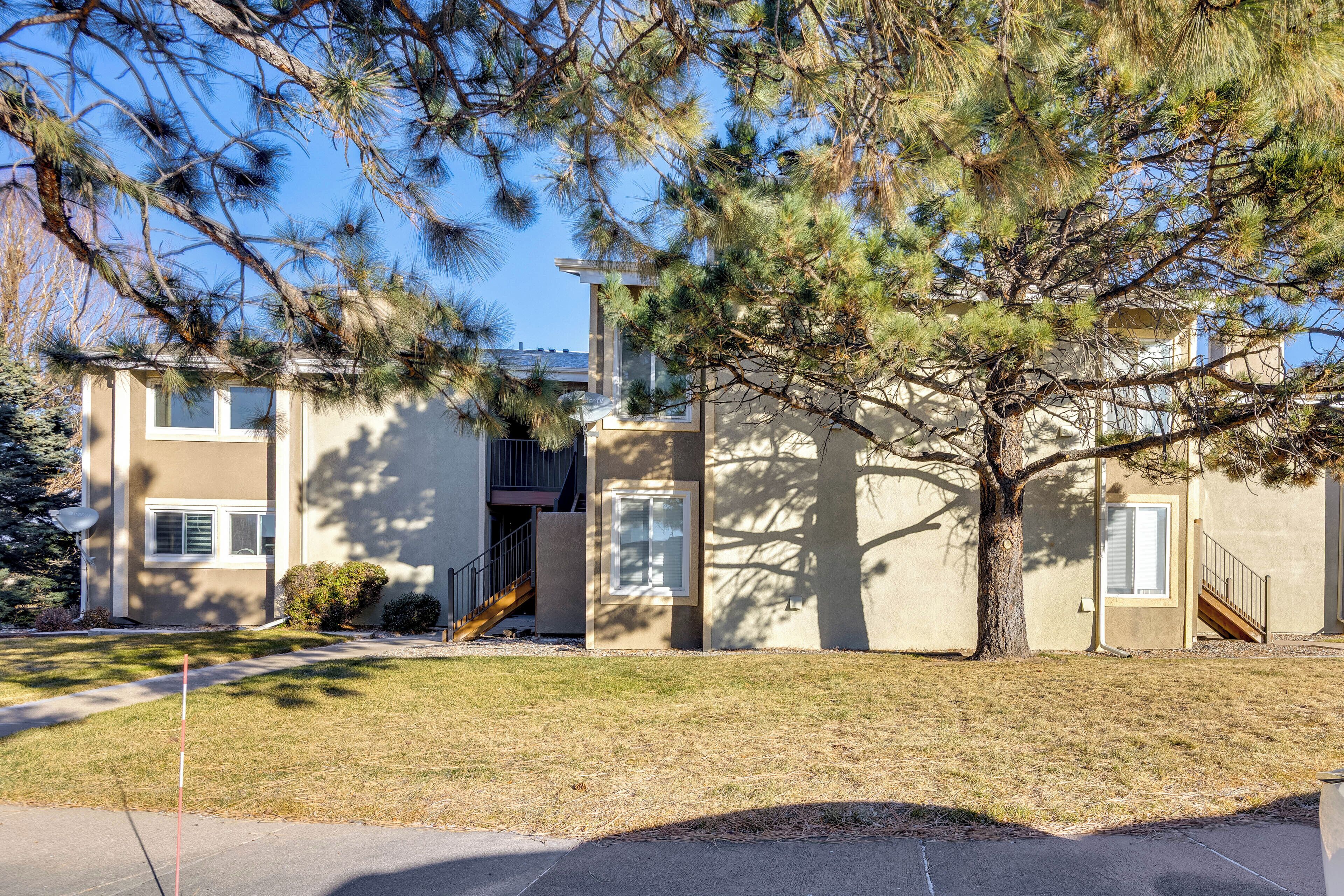 A two-story residential building with a front yard, a tree, and a clear sky.