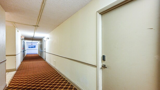 Ein Hotelgang mit Teppichmuster, einer weißen Tür und einem Ausgangsschild.