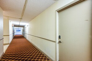A hotel hallway with a patterned carpet, a white door, and an exit sign. - Walk to Beach: Luxe Harbor-view Condo in Naples! (Naples)