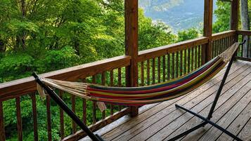 Una hamaca en una cubierta de madera con vista a un bosque y montañas.
