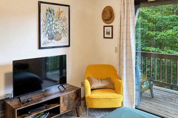 A living room with a flat-screen TV on a wooden stand, a yellow armchair with a cushion, and a framed floral painting on the wall. - Fall Colors! Mtn-view Deck Maggie Valley (Maggie Valley)
