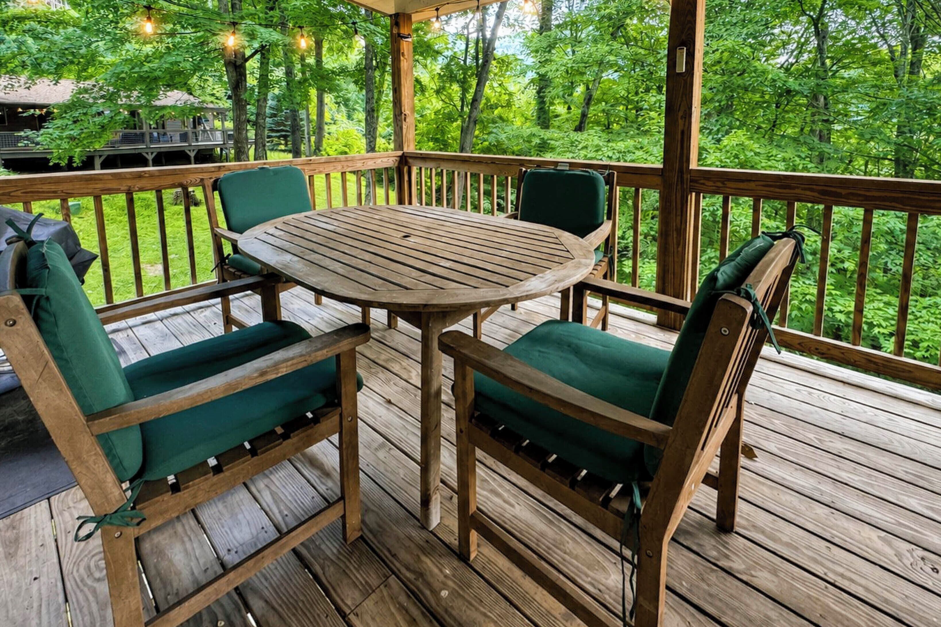 A wooden deck with a round table and four chairs, surrounded by a wooden railing.