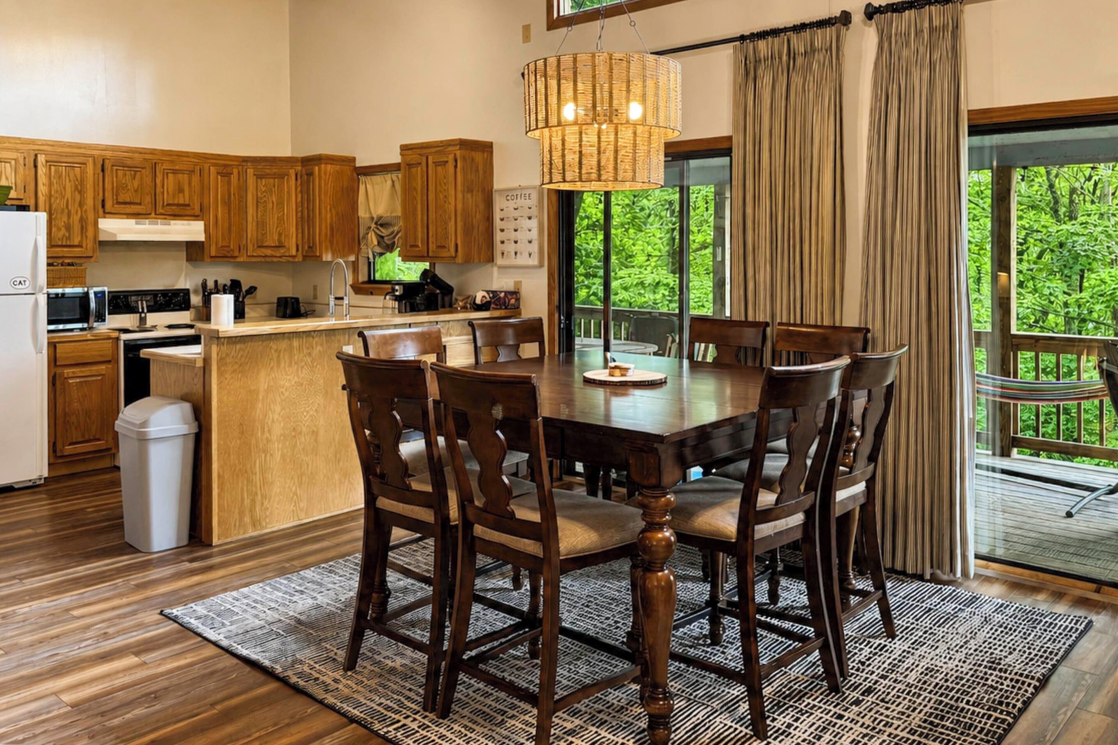 A modern kitchen with wooden cabinets, a central island with seating, and a large window offering a view of greenery.