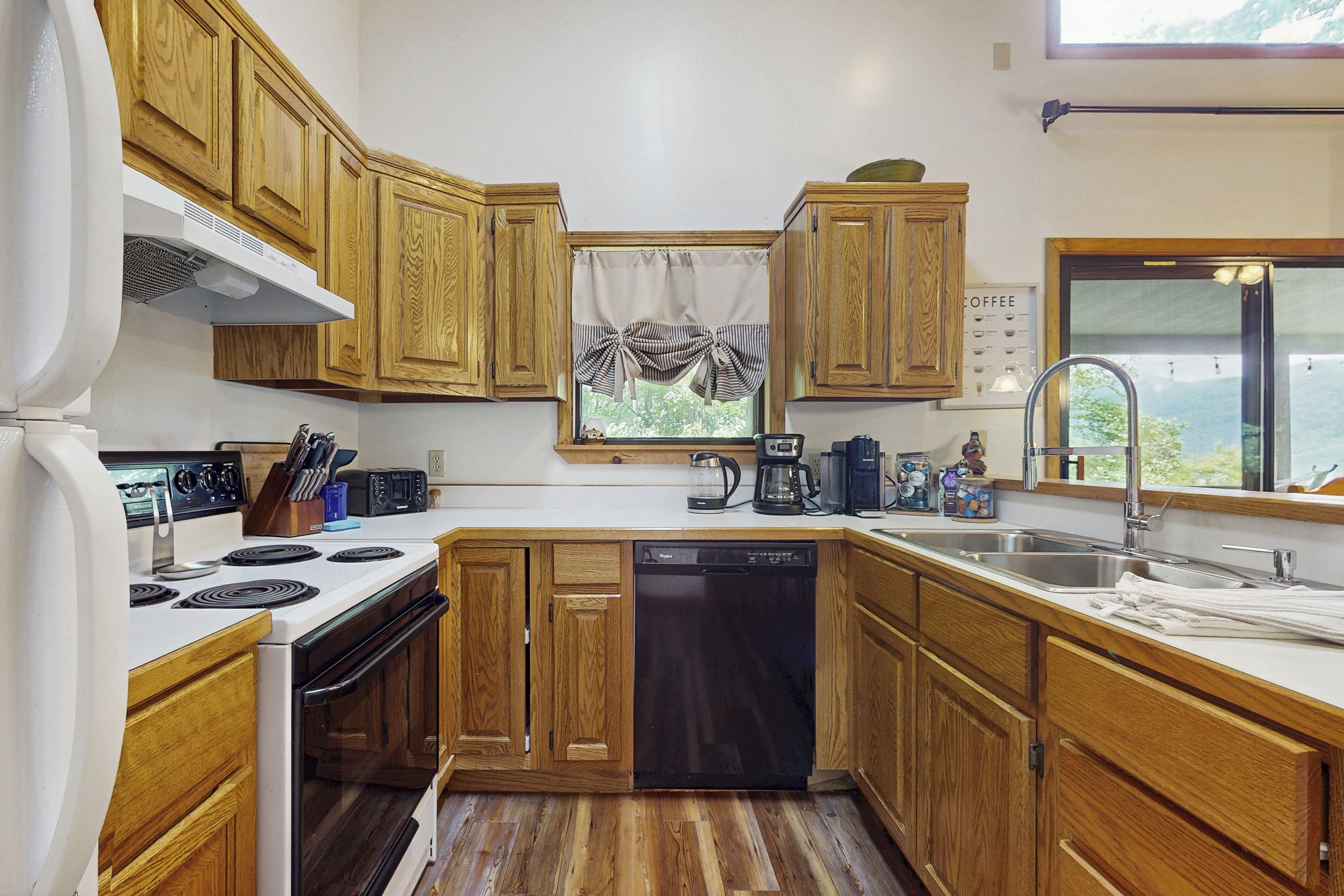 A kitchen with wooden cabinets, a dishwasher, a stove, and a window with curtains.