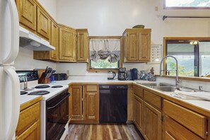 Una cocina con armarios de madera, lavavajillas, estufa y una ventana con cortinas.