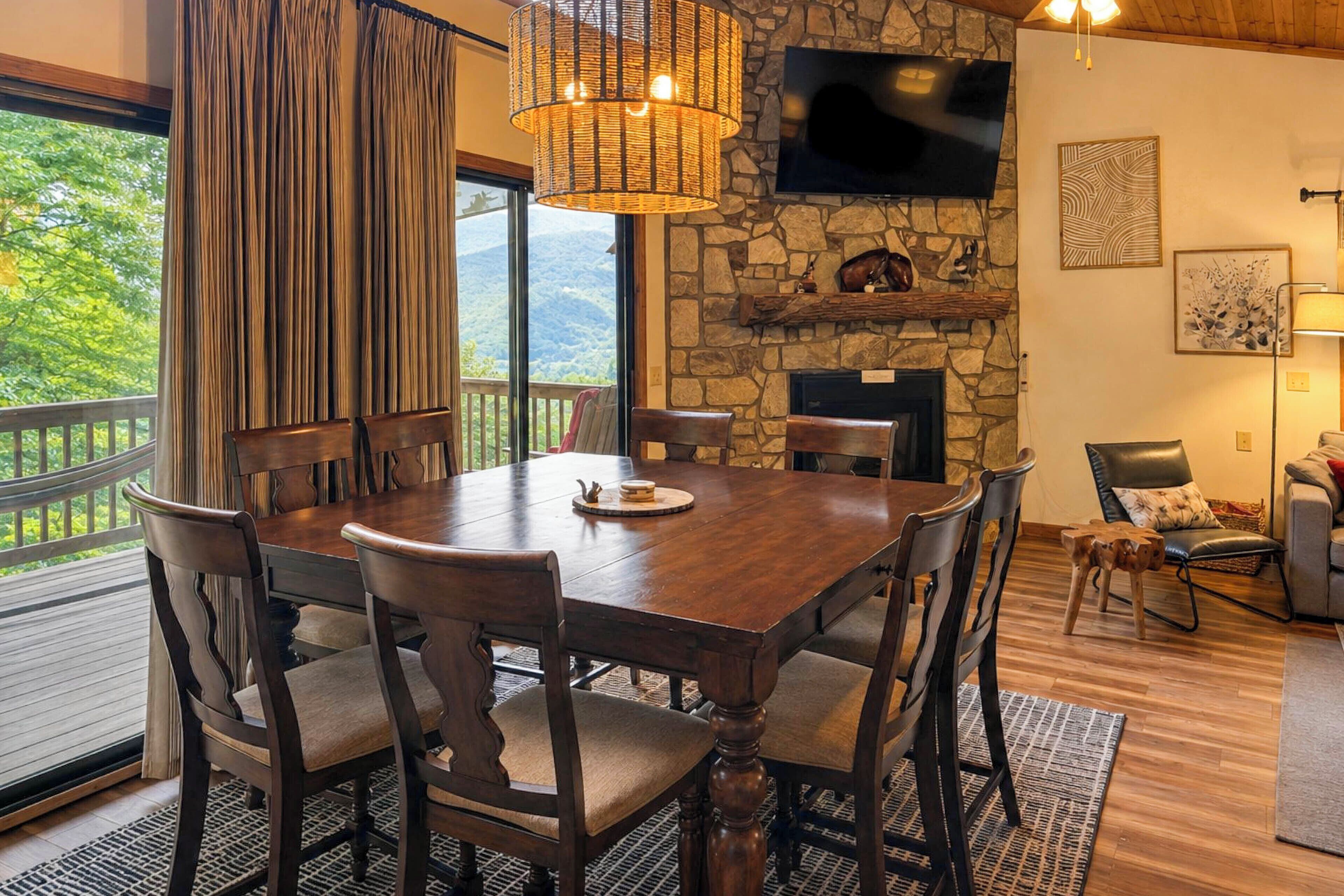 A dining area with a stone fireplace, a television mounted above it, and a view of the outdoors.