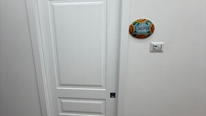 Eine weiße Tür mit schlichtem Design, eine kleine Schild mit dem Wort „Cucina“ an der Wand und ein Lichtschalter.