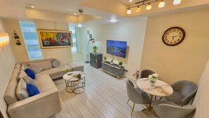 Una sala de estar moderna con un sofá, una mesa de centro y sillas, un televisor de pantalla plana, plantas decorativas y obras de arte en las paredes.