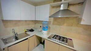 Cocina compacta con armarios blancos, pileta de acero inoxidable, estufa a gas y dispensador de agua.