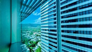 Un edificio de gran altura con fachada de vidrio moderna y vistas a un paisaje urbano con zonas verdes y montañas al fondo.