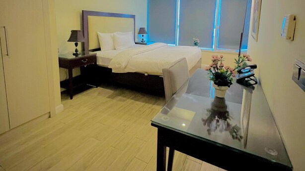Una habitación de hotel moderna con una cama, mesita de noche, lámpara y una pequeña mesa con un florero.