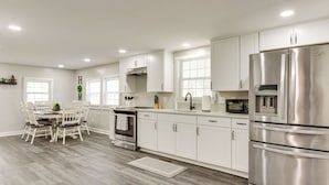 A modern kitchen with white cabinets, stainless steel appliances, and a dining area with a wooden table and chairs. - Secluded Getaway on 40 Acres in Lawrenceburg! (Lawrenceburg)