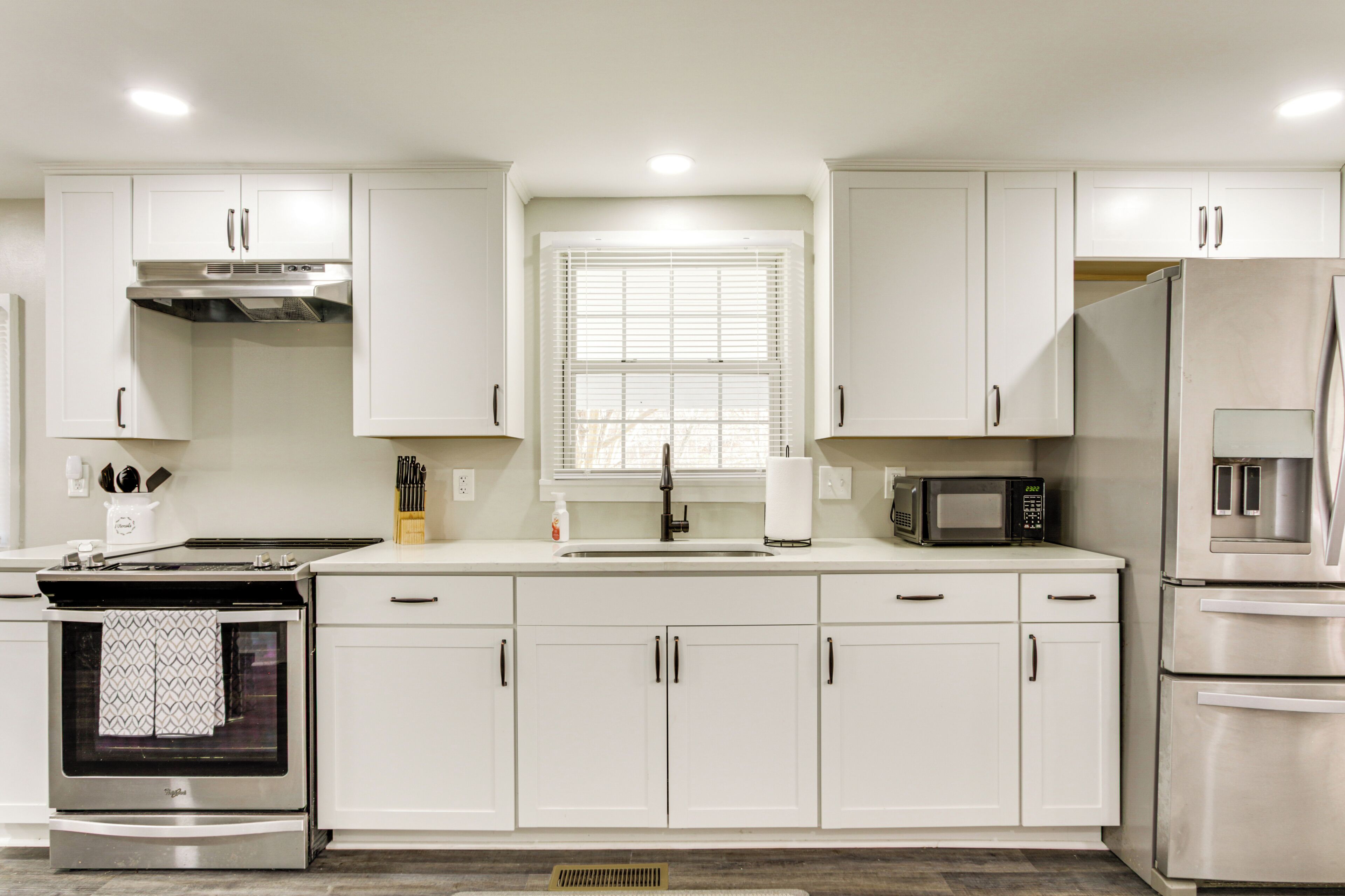 Una cocina moderna con armarios blancos, electrodomésticos de acero inoxidable y una ventana con persianas.