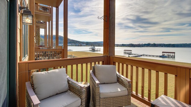A balcony with wicker chairs and a table, overlooking a calm lake with docks and a distant shoreline. - Lakefront Condo 3 Mi to Historic Guntersville! (Guntersville)