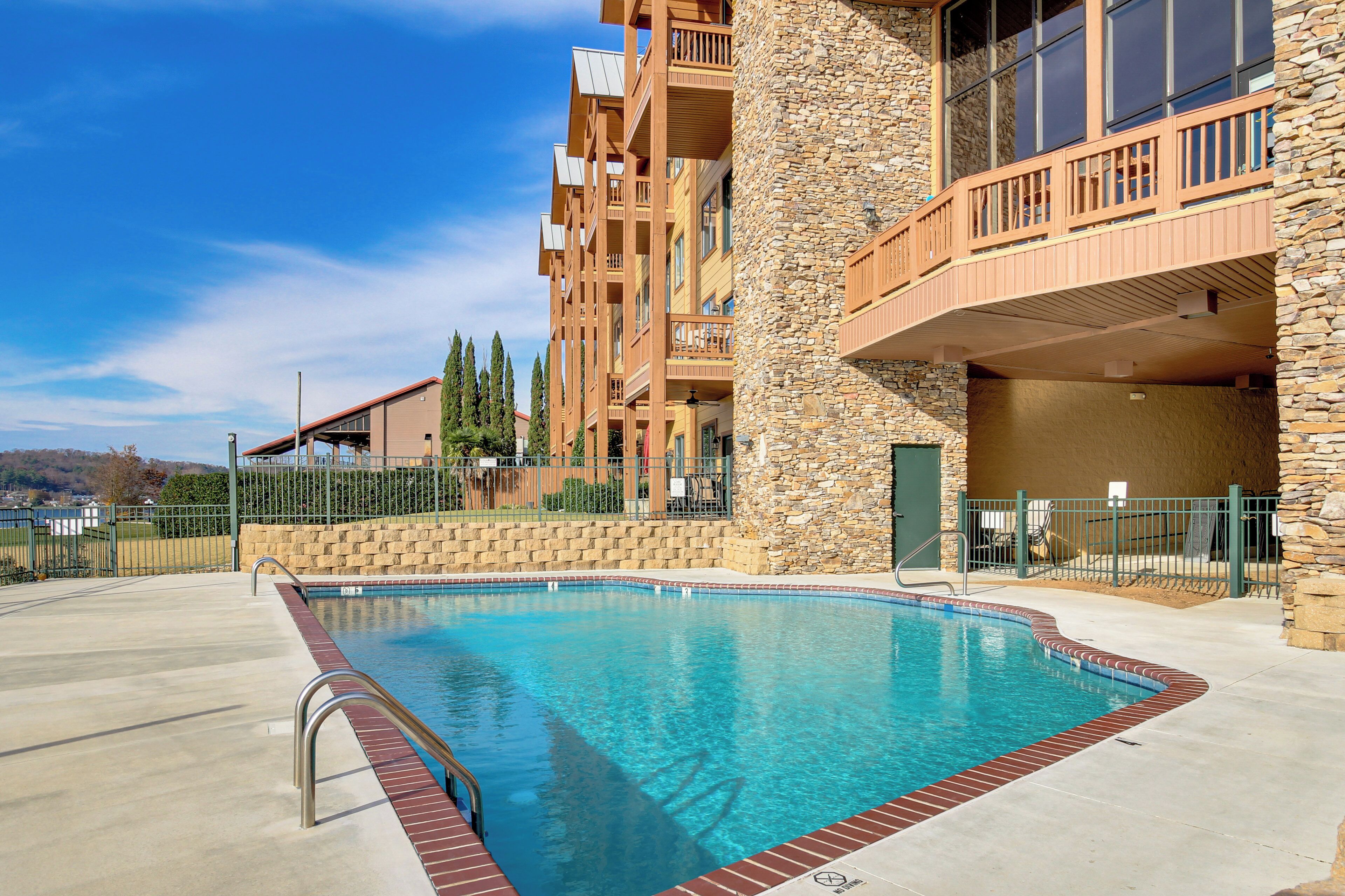 A swimming pool with a stone wall and wooden balconies, surrounded by a fenced area.