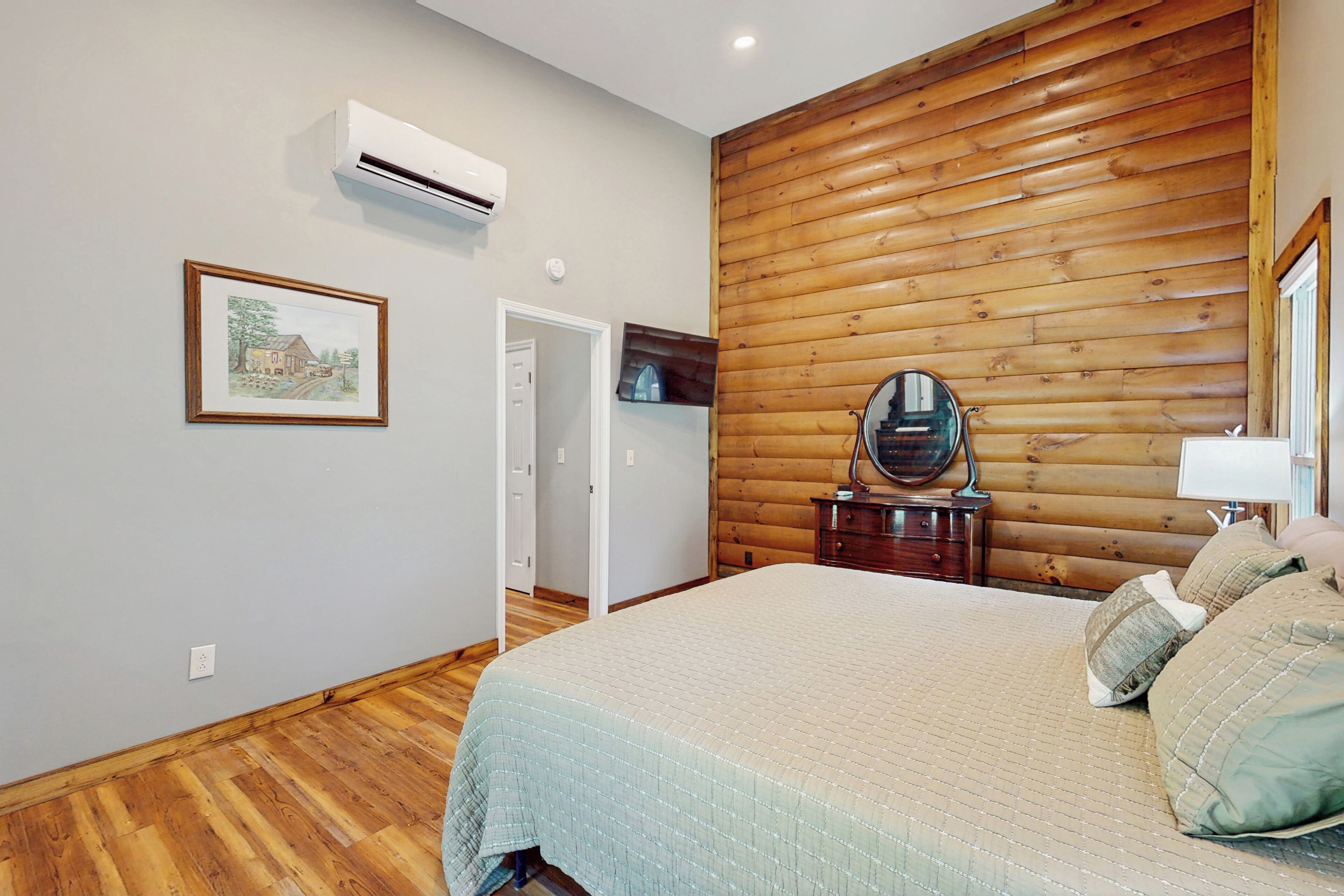 A bedroom with a wooden wall panel, a bed with a quilt, a dresser with a mirror, and an air conditioning unit on the wall.