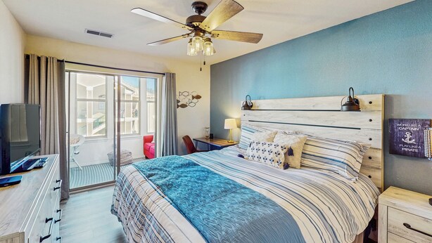 A bedroom with a bed, a ceiling fan, a TV, a desk, and a sliding glass door to a balcony. - 2BR Poolside Condo w/ Sunroom, Close to Marina (Hollister)