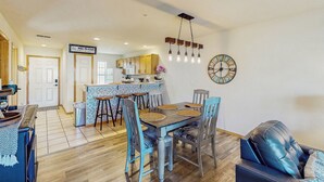 A dining area with a wooden table and chairs, a kitchen in the background, and a clock on the wall. - 2BR Poolside Condo w/ Sunroom, Close to Marina (Hollister)