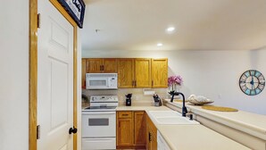 A modern kitchen with wooden cabinets, a white stove, a microwave, a sink, and a clock on the wall. - 2BR Poolside Condo w/ Sunroom, Close to Marina (Hollister)