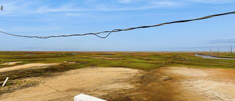 A view from a balcony with a railing, overlooking a landscape with patches of grass and dirt, and a clear blue sky.