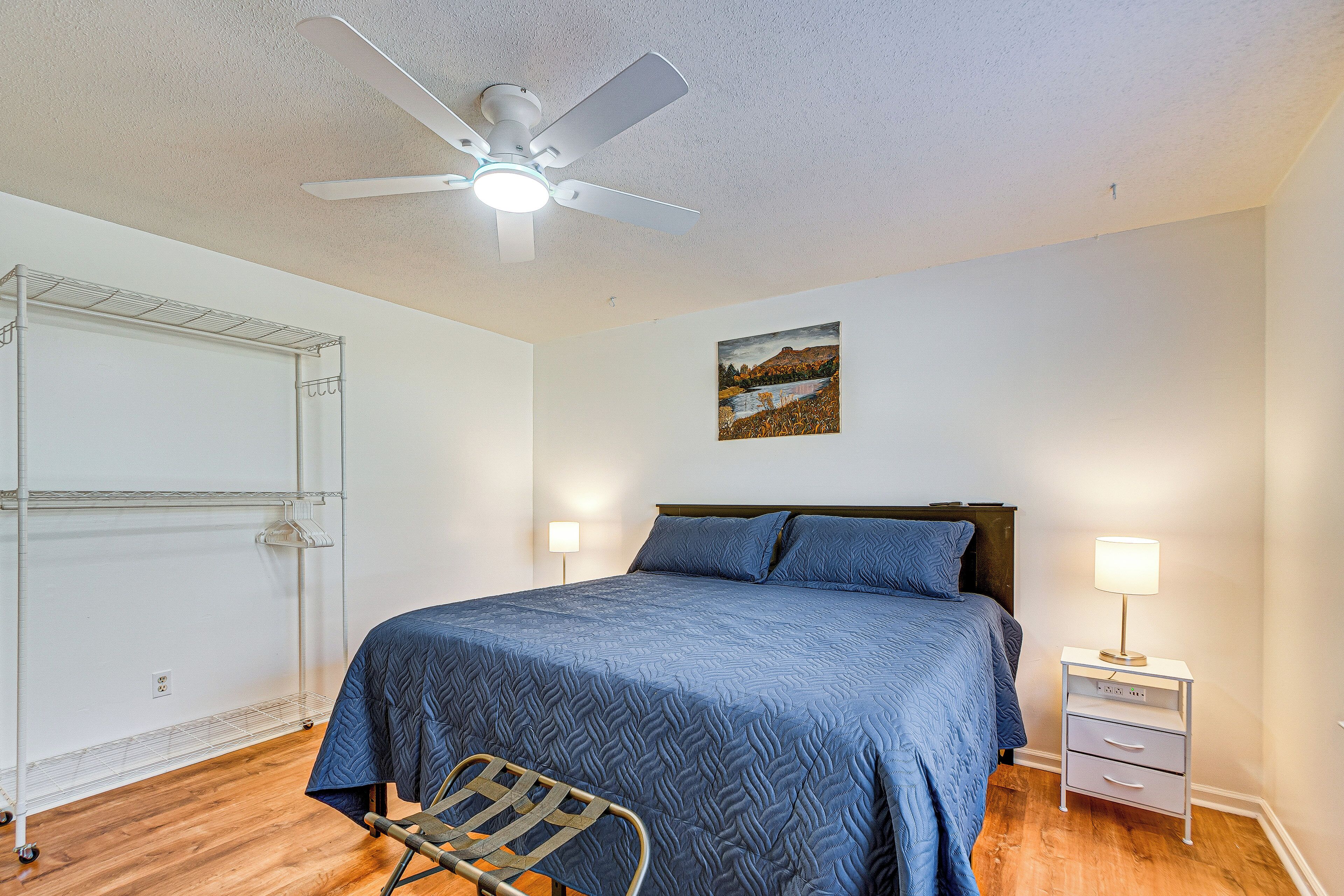 A bedroom with a bed, a nightstand, a chair, a ceiling fan, and a wall-mounted shelf.