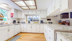 A modern kitchen with white cabinets, a large window, and a wooden floor. - Creekside Escape w/ Private Hot Tub in Shingletown (Shingletown)