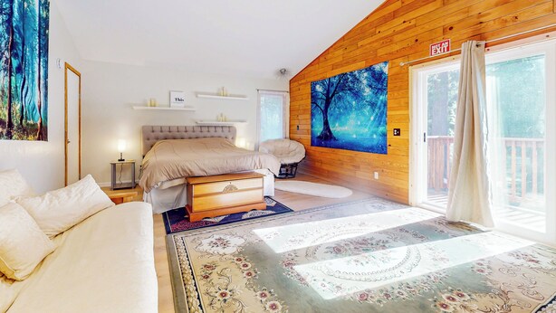 A bedroom with a bed, bedside tables, a nightstand, a dresser, a wall-mounted TV, and a large window with curtains. - Creekside Escape w/ Private Hot Tub in Shingletown (Shingletown)