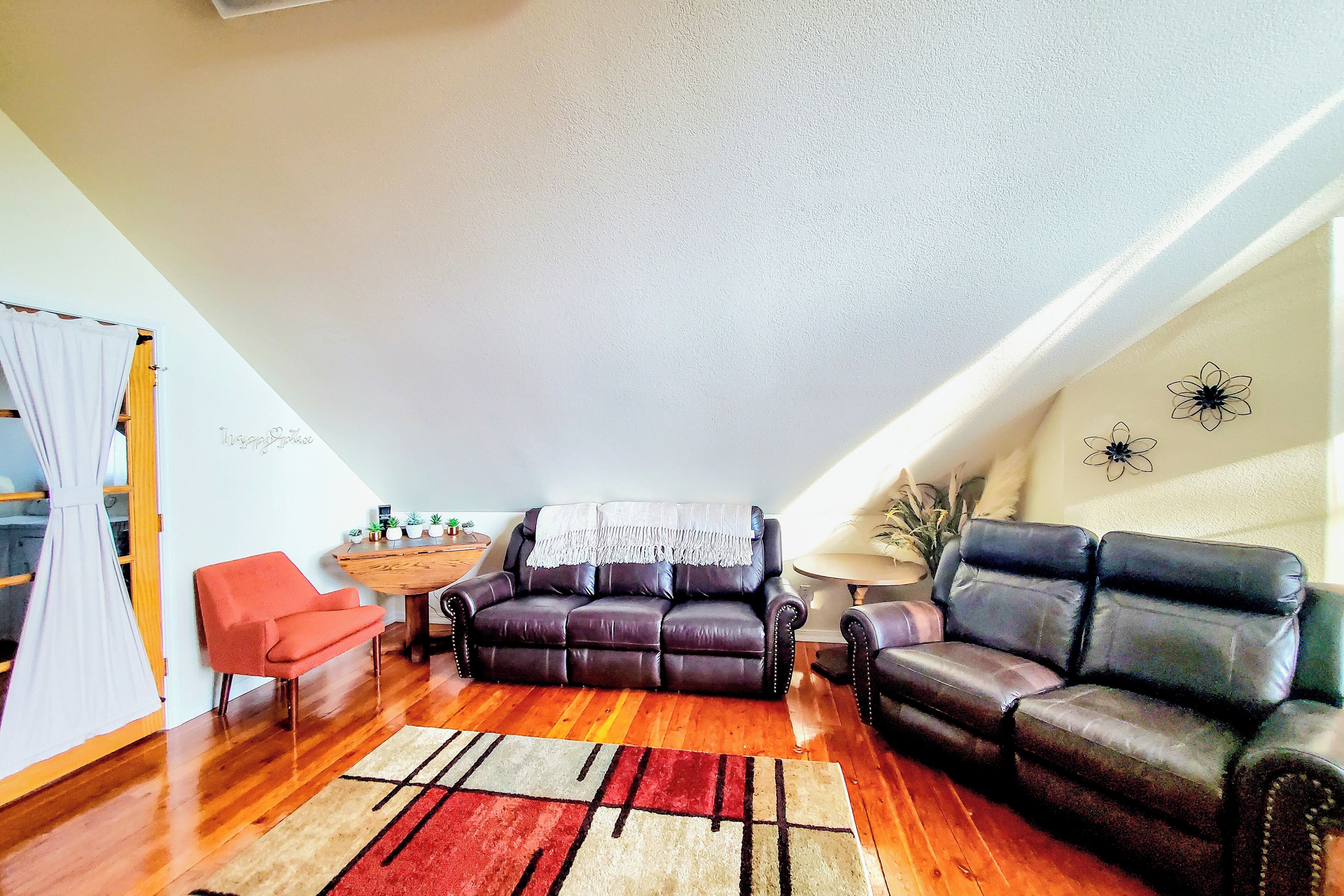 Een woonkamer met een bruine leren bank, een rode fauteuil en een houten salontafel.