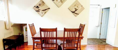 A dining area with a wooden table and chairs, a bench, and three wall-mounted floral paintings.