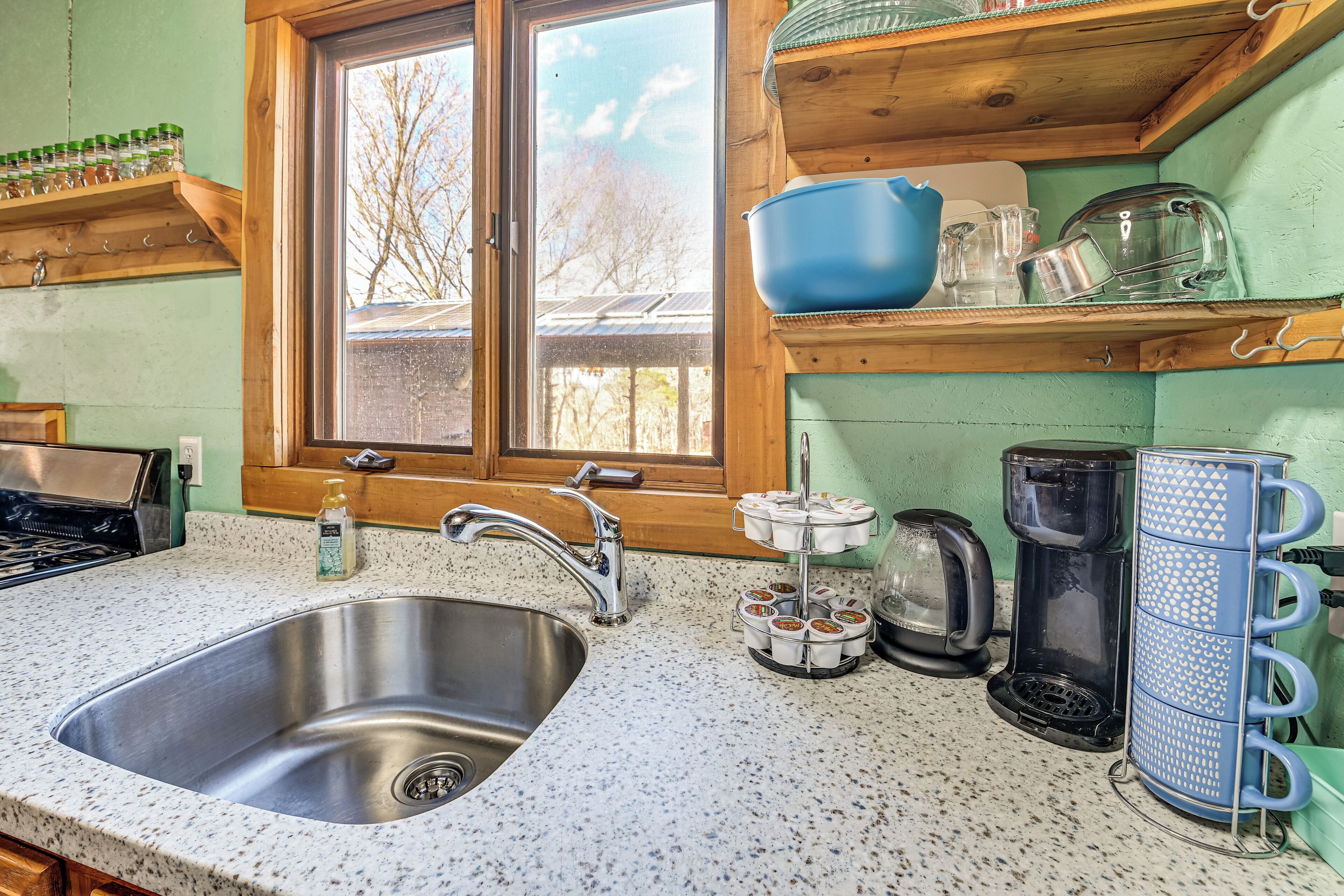 A kitchen with a stainless steel sink, wooden shelves, a window, and various kitchen appliances.