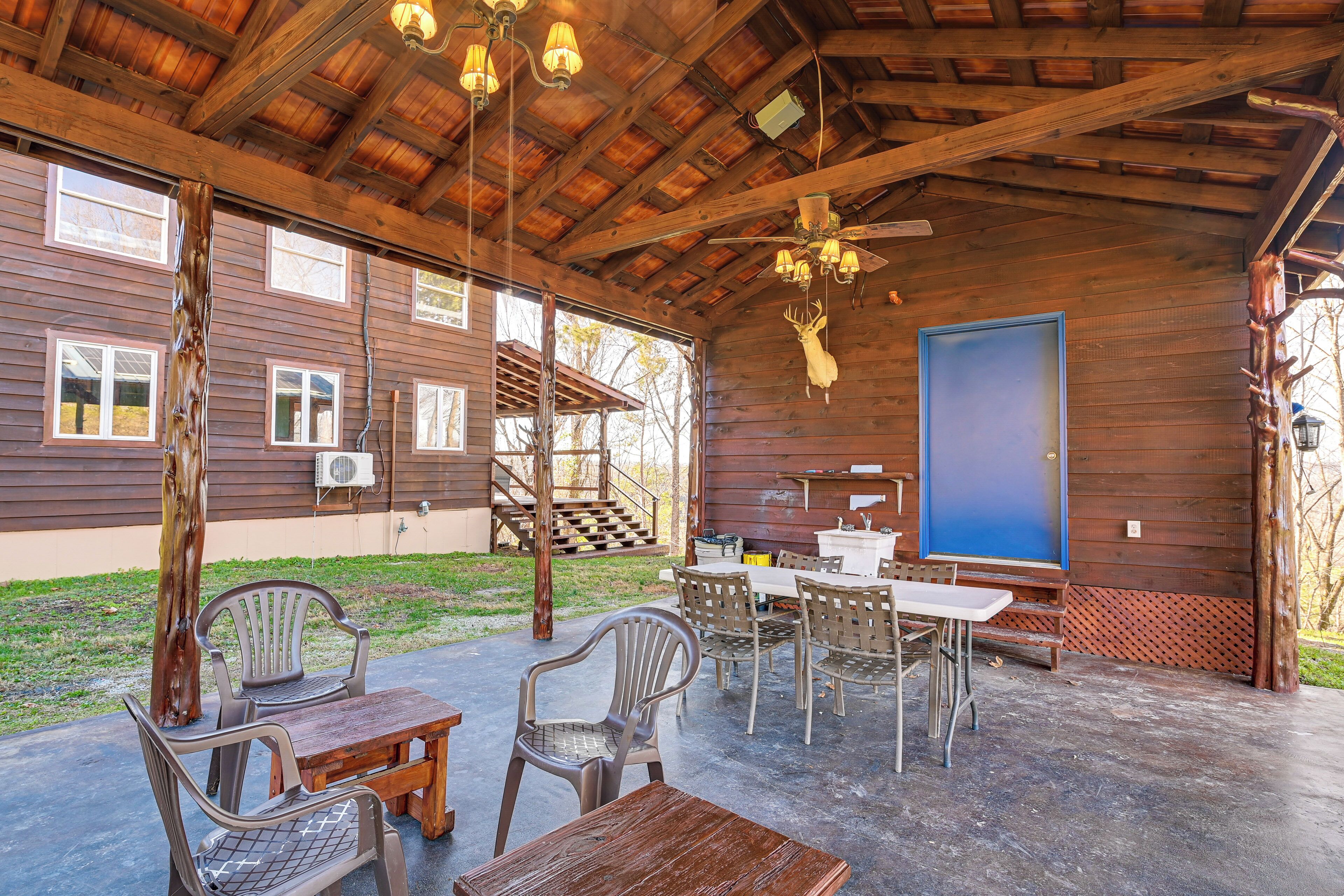 Un espace extérieur abrité, aménagé avec des meubles en bois, un ventilateur de plafond et une grande porte bleue.