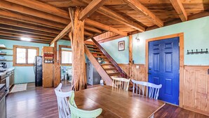 Una cocina rústica con vigas de madera, una mesa de comedor con sillas, una puerta azul y una escalera que sube a otro nivel.