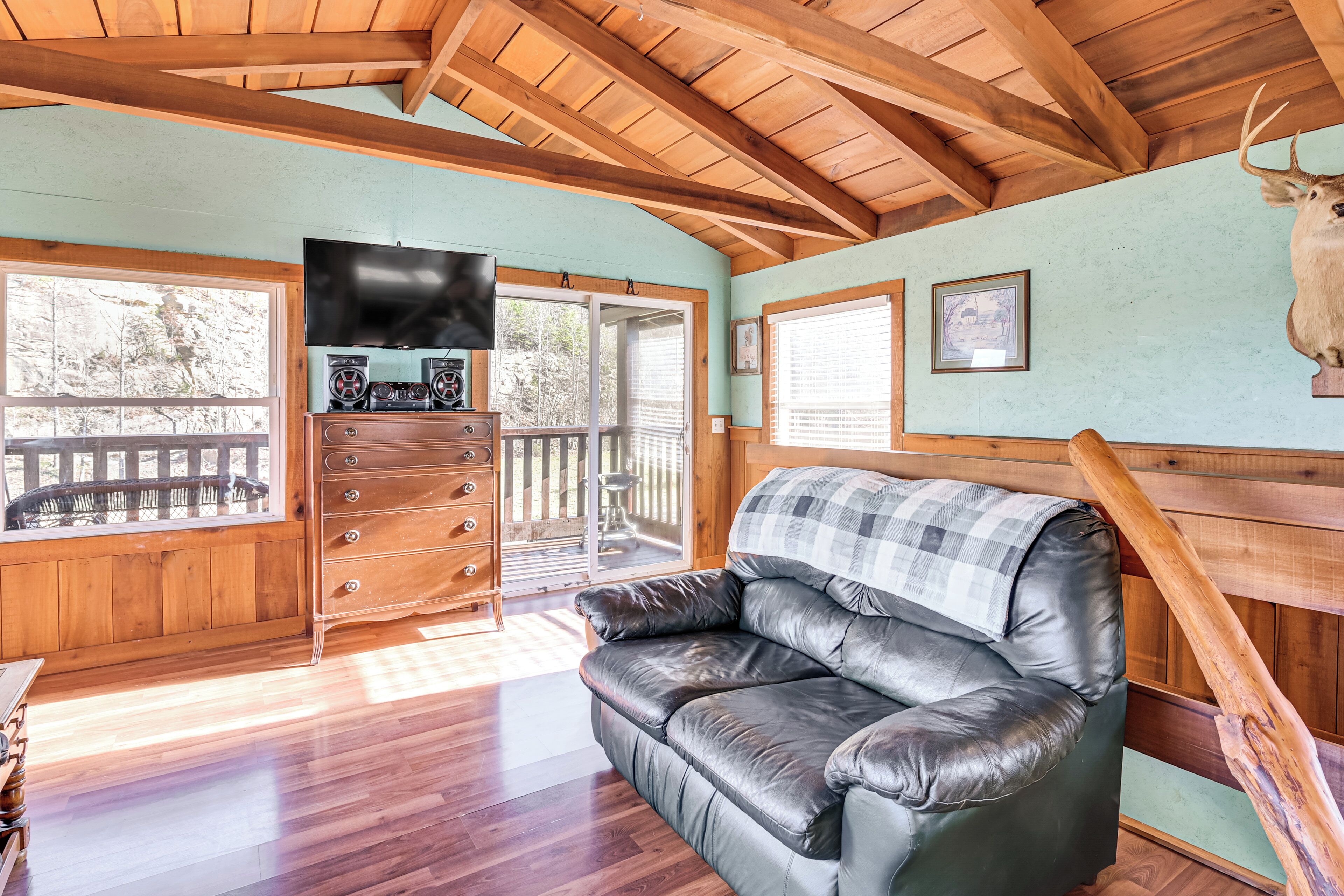L’intérieur chaleureux d’un chalet avec un canapé en cuir, des poutres en bois au plafond, un téléviseur et une tête de cerf fixée au mur.