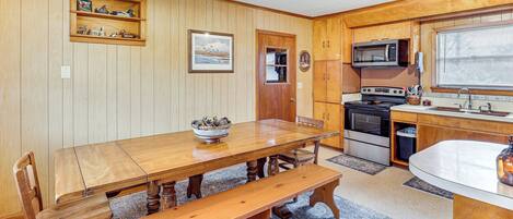 A wooden dining table with benches, a kitchen area with a microwave and stove, and a window with blinds.