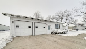 A residential garage with two white doors, a concrete driveway, and a snow-covered landscape. - Spacious Retreat w/ Private Yard & Deck in Roscoe! (Roscoe)