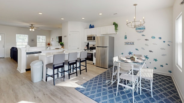 A modern kitchen with white cabinetry, stainless steel appliances, and a dining area with white chairs and a blue rug. - 4BR Lakefront Retreat w/ Furnished Deck, Dock (Salisbury)