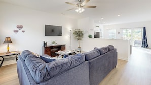 A modern living room with a grey sofa, a flat-screen TV, a ceiling fan, and a dining area with a table and chairs. - 4BR Lakefront Retreat w/ Furnished Deck, Dock (Salisbury)