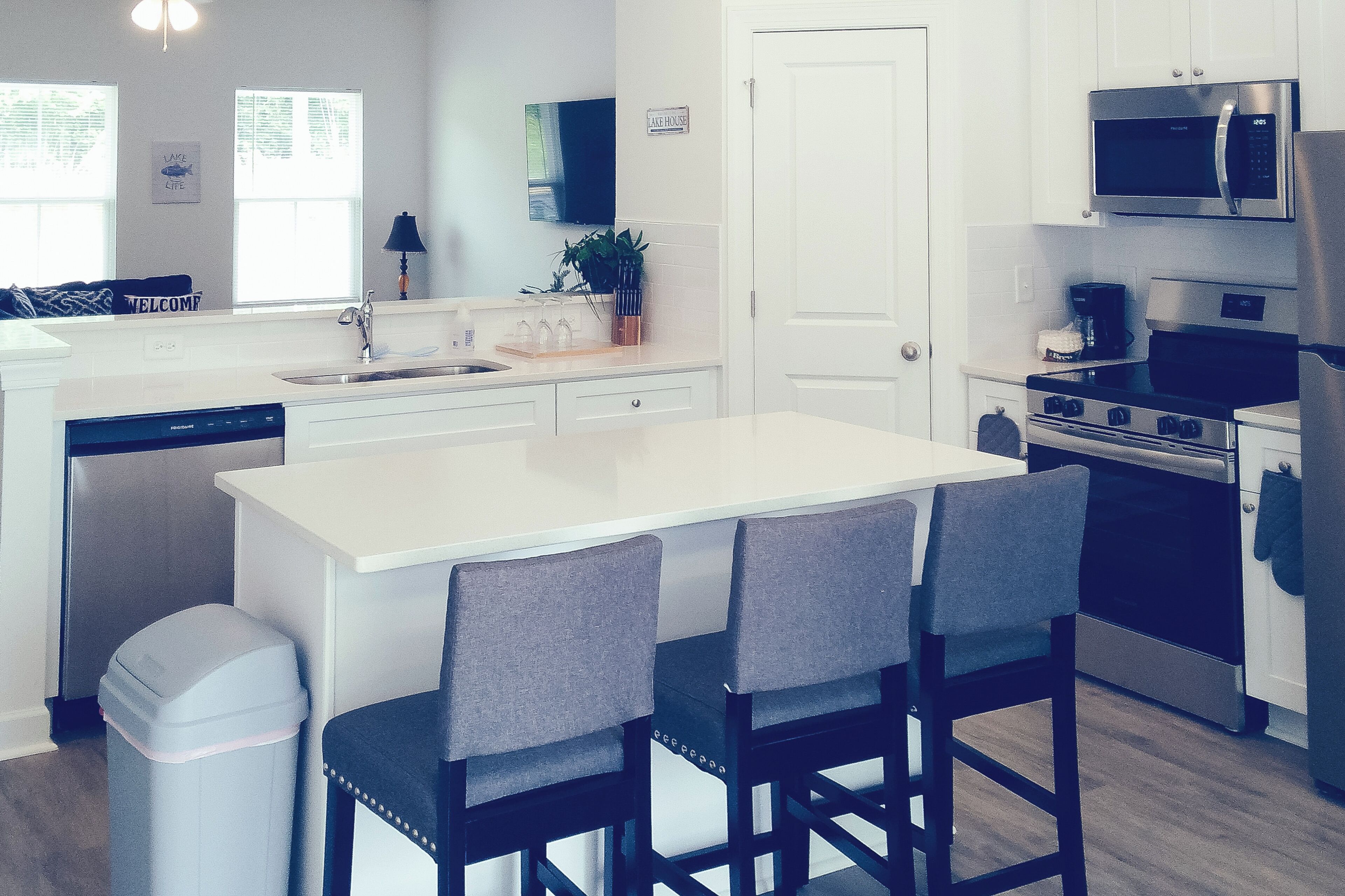 A modern kitchen with a central island, bar stools, a dishwasher, a stove, and a microwave.
