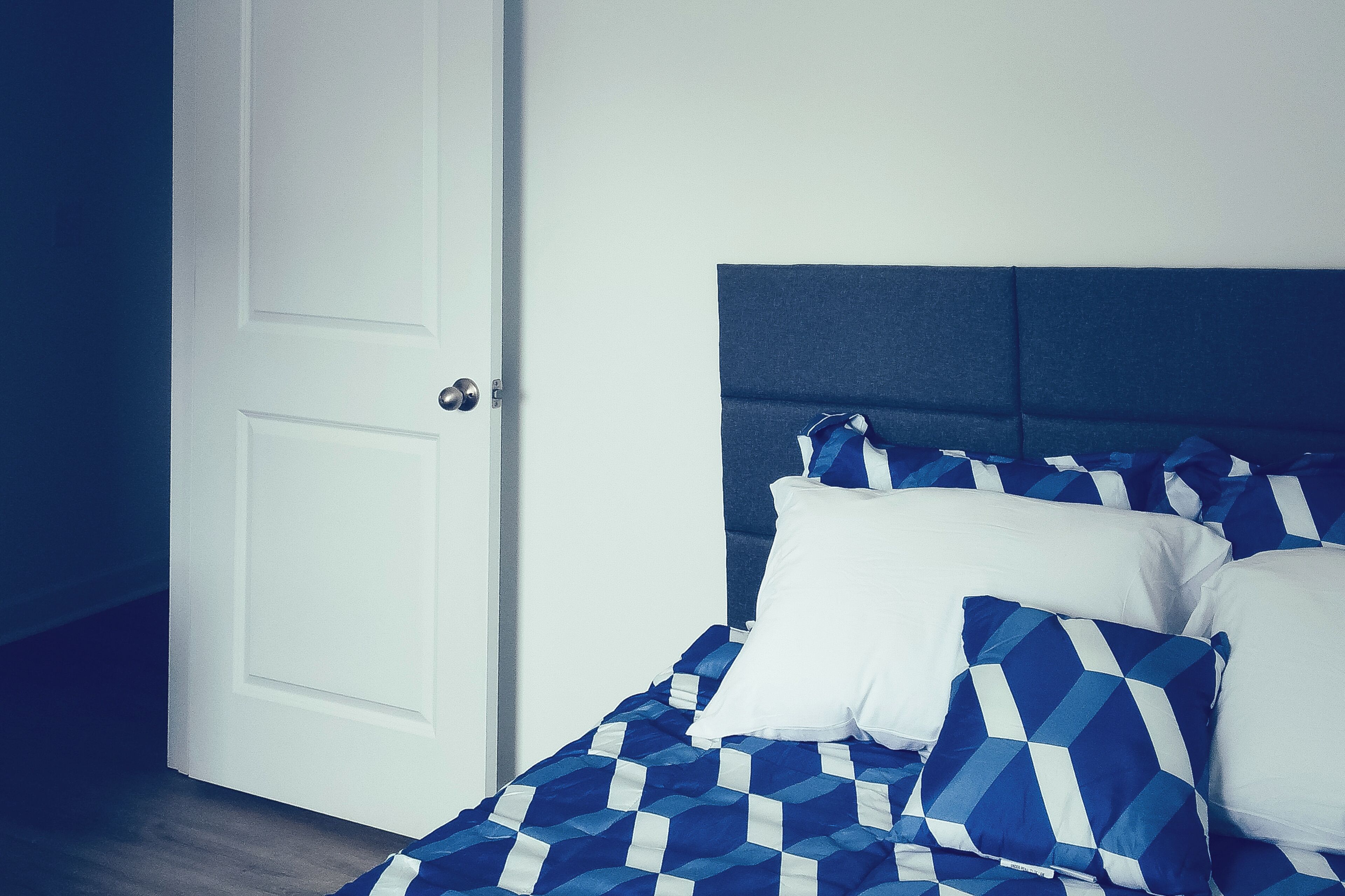 A bedroom with a bed, white door, and blue and white bedding.