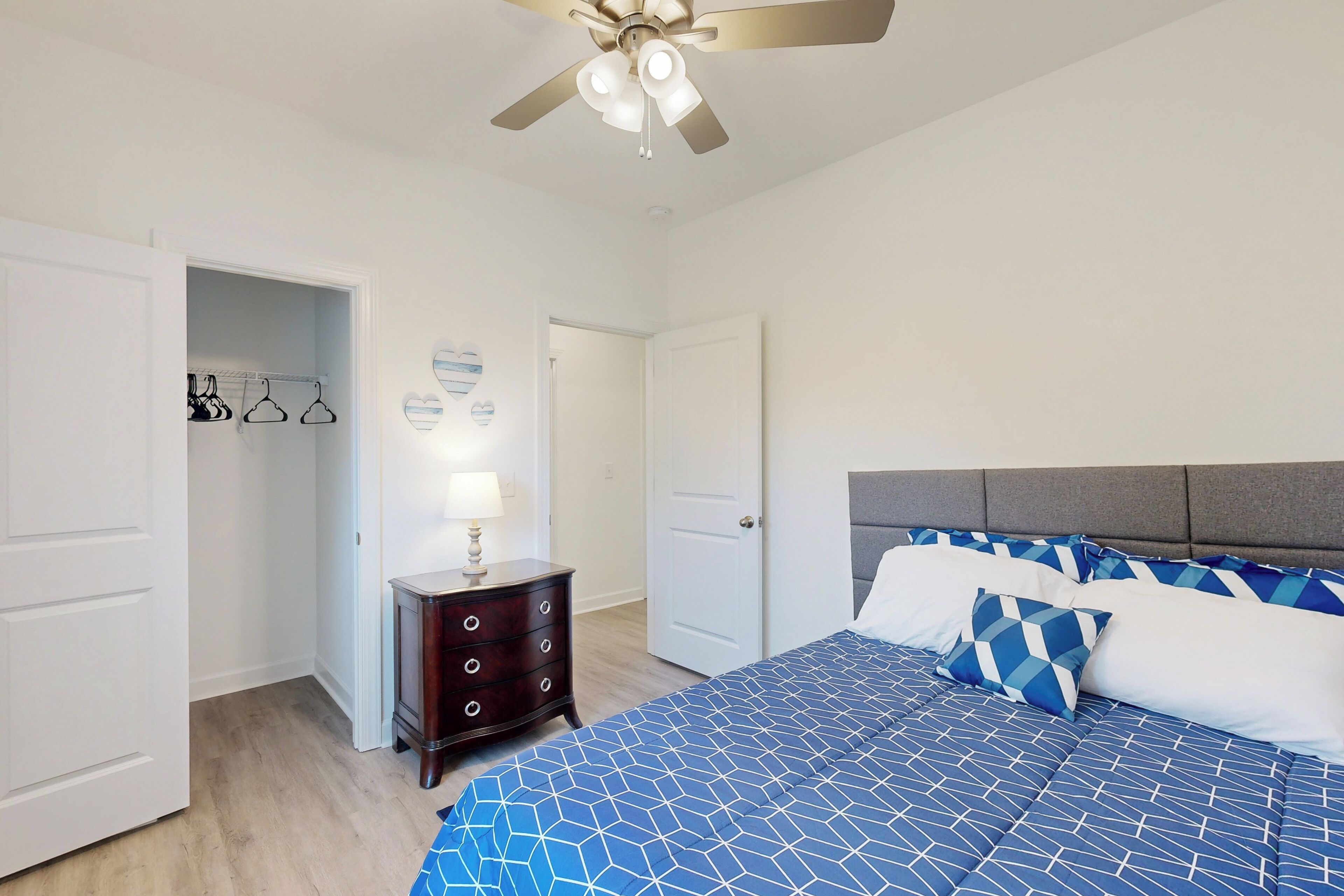 A bedroom with a bed, a nightstand, a dresser, a ceiling fan, and a door leading to a closet.