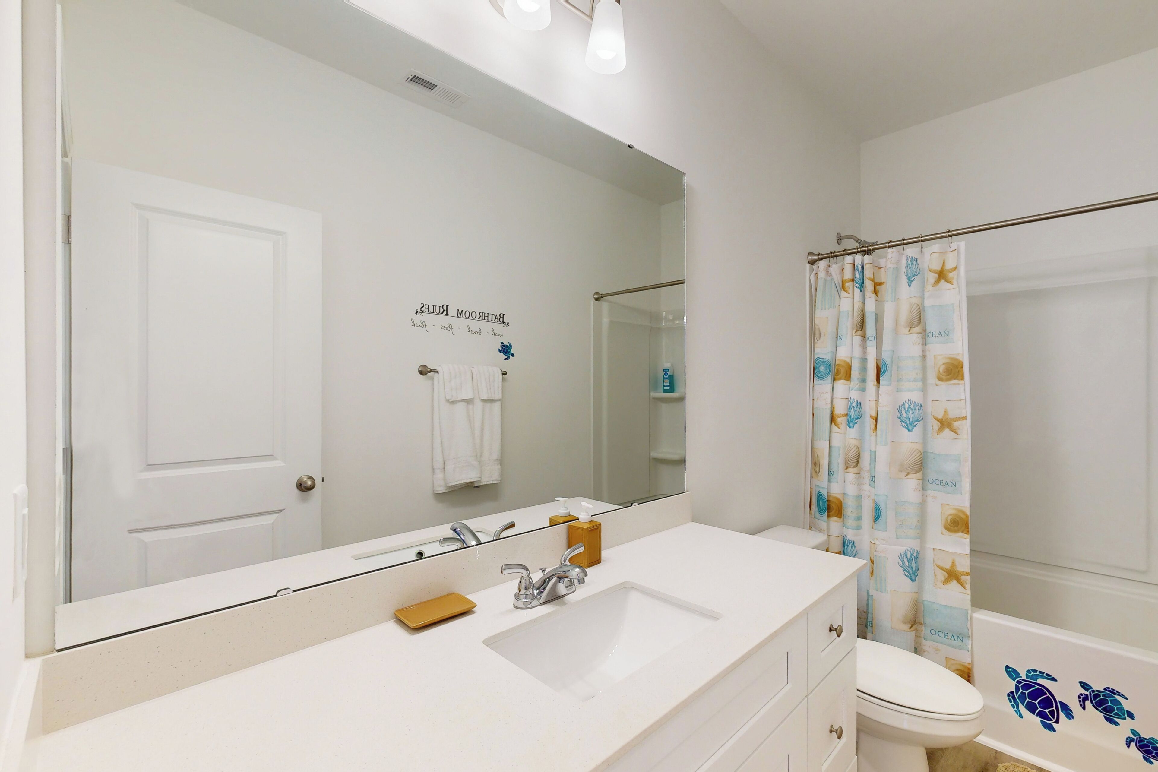 A bathroom with a white sink, a mirror, a toilet, and a shower curtain with a sea turtle design.