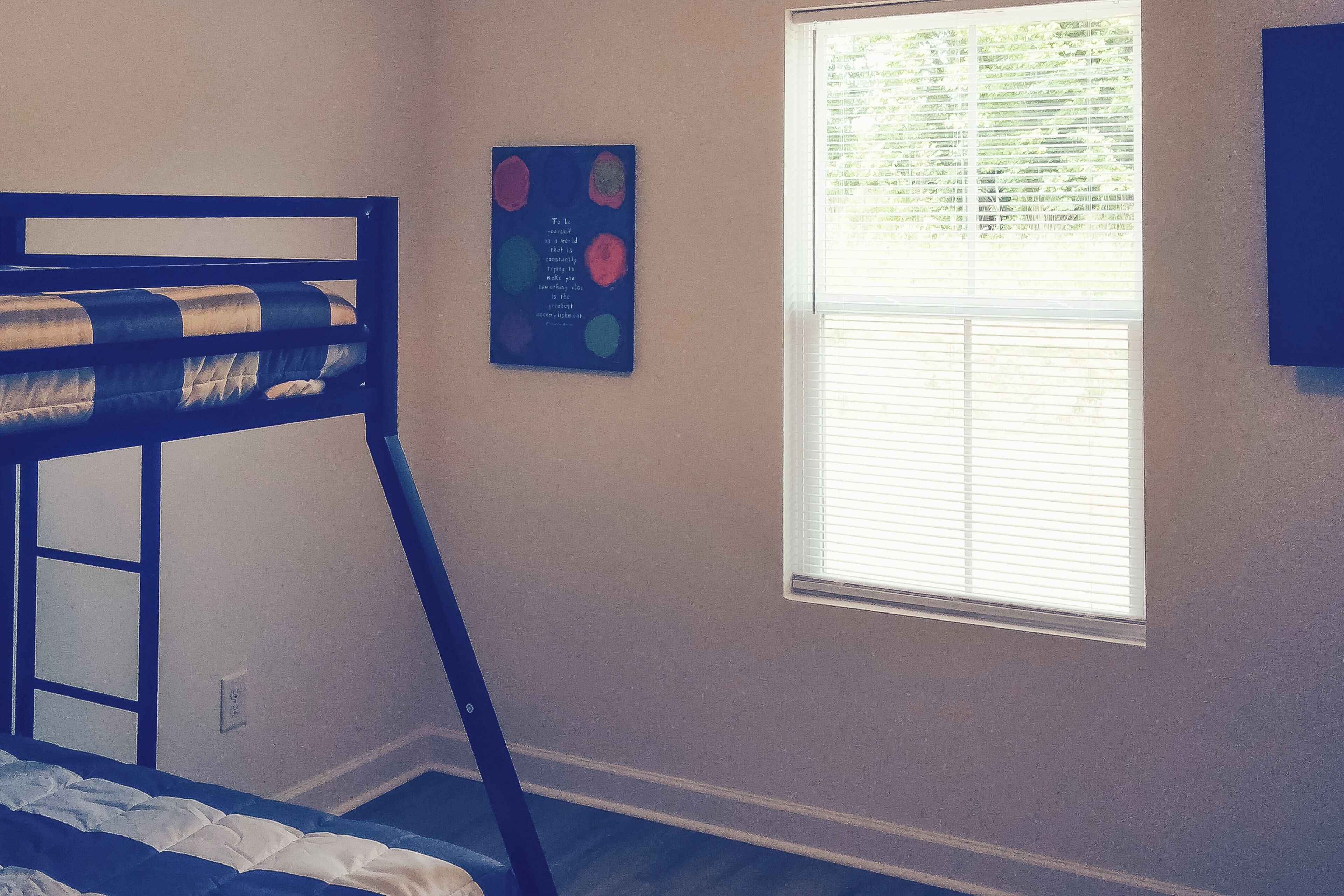 Una cama litera en una habitación con ventana, una obra de arte colgada en la pared y una puerta.