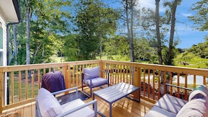 A wooden deck with outdoor furniture, including a table and two chairs, overlooking a lush garden and a pond. - 4BR Lakefront Retreat w/ Furnished Deck, Dock (Salisbury)