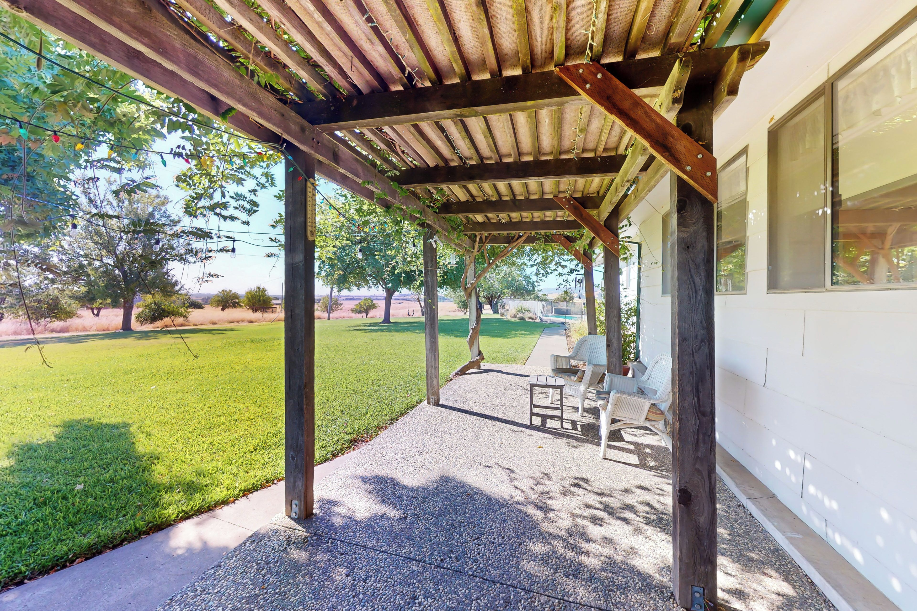 A covered patio area with a concrete floor, wooden beams, and a view of a grassy yard and trees.