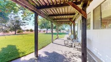A covered patio area with a concrete floor, wooden beams, and a view of a grassy yard and trees.