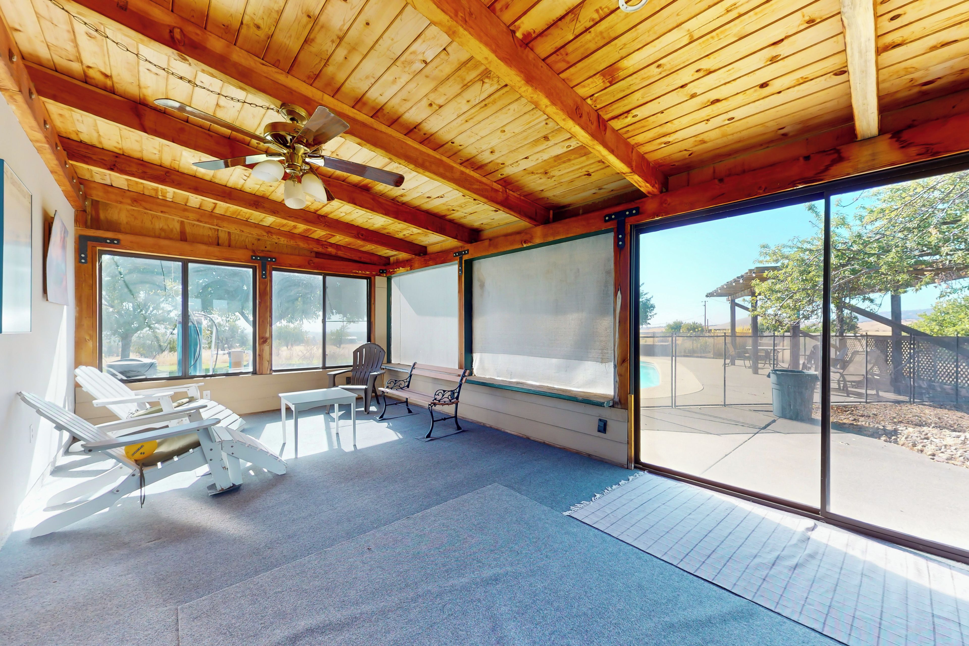 Una sala de estar con ventanales amplios, ventiladores de techo y mobiliario para exteriores.