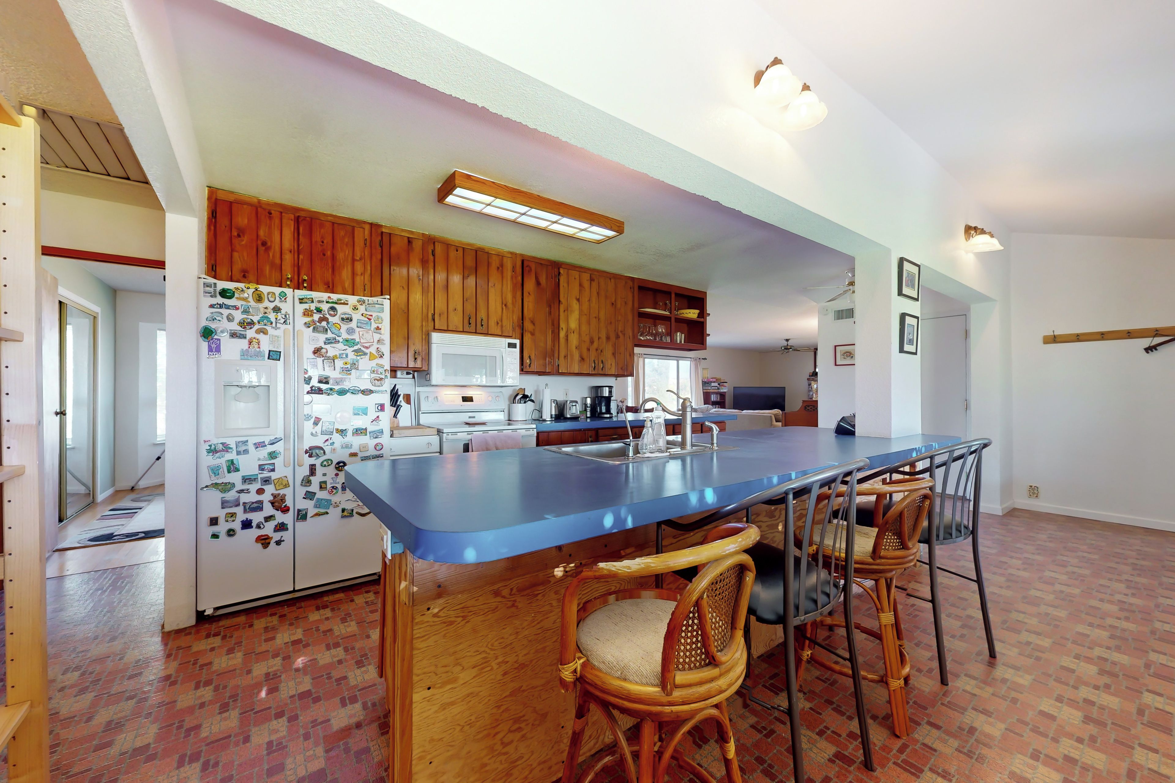 A kitchen with wooden cabinets, a blue countertop, and a bar seating area with wicker chairs.