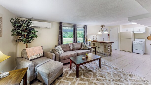 A living room with a sofa, a coffee table, and a rug. There is a kitchen area with cabinets and appliances. - River Access! Couples Retreat on Working Homestead (Woodburn)