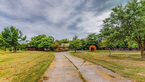 A park with a concrete pathway, trees, and buildings in the background. - River Access! Couples Retreat on Working Homestead (Woodburn)